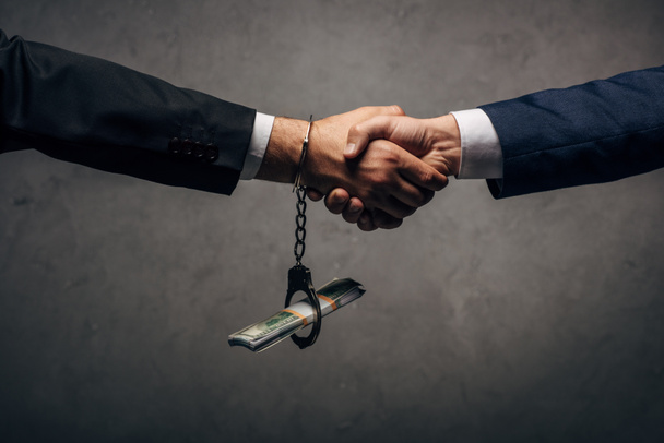 cropped view man in handcuffs shaking hands with business partner on grey  - Zdjęcie, obraz
