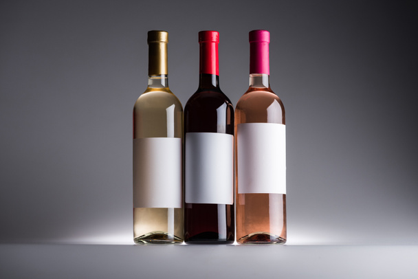 garrafas de vinho tinto, branco e rosa com rótulos em branco no fundo escuro com luz traseira
 - Foto, Imagem