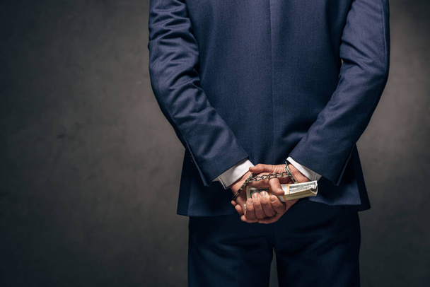 cropped view of handcuffed man in formal wear holding bribe on grey  - Φωτογραφία, εικόνα
