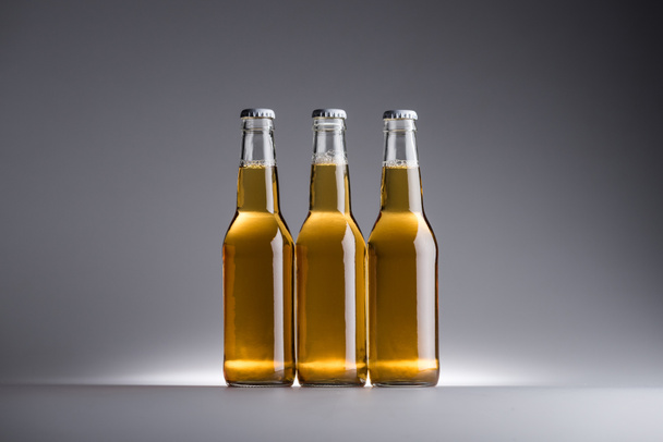 three glass bottles with beer in row on grey background with copy space - 写真・画像
