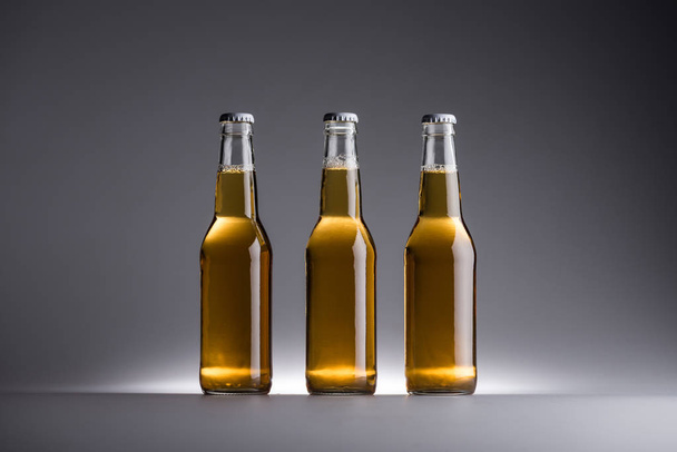 three glass bottles with beer in row on grey background - 写真・画像