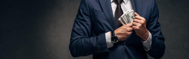 Panoramaaufnahme eines Geschäftsmannes im Anzug, der Bargeld in der Tasche auf grau legt  - Foto, Bild