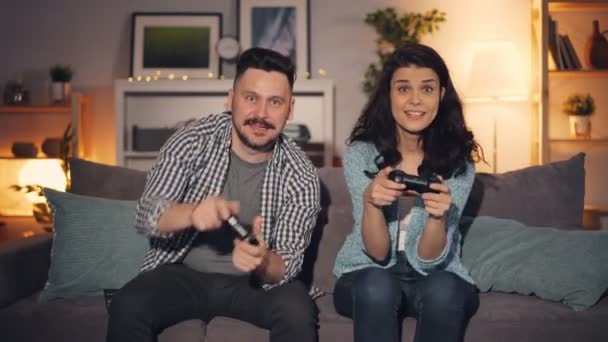Cute couple husband and wife playing video games at home, joyful man winning - Filmati, video