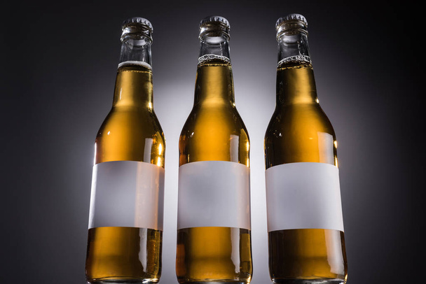 low angle view of glass bottles with beer and labels on dark background with back light - Foto, immagini