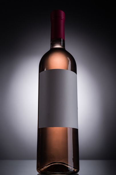 low angle view of bottle with rose wine and blank label on dark background with back light - Photo, Image