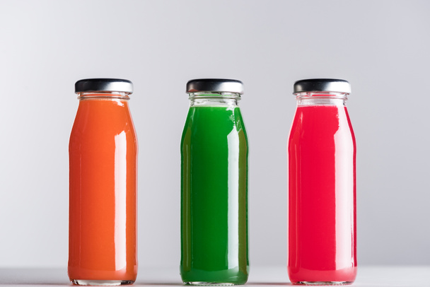 row of glass bottles with multicolored juice isolated on grey - Photo, Image