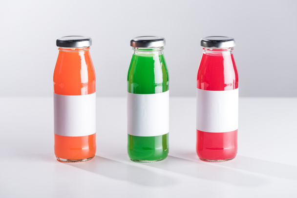 row of glass bottles with multicolored liquid and white labels isolated on grey - Photo, Image