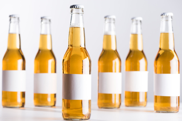 selective focus of glass beer bottles with blank white labels isolated on grey - Photo, Image