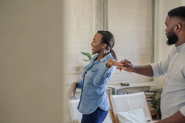 Affectionate young African American couple laughing while dancing hand in hand together in their living room at home - Photo, Image