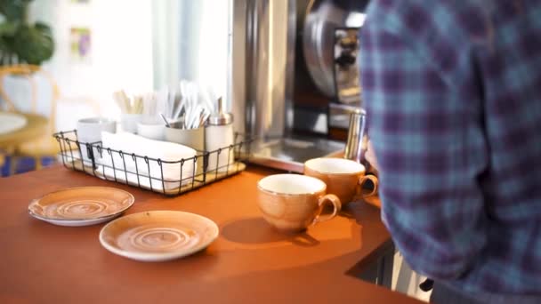 Oldalnézetből egy profi Barista üzembe friss tejet a Dobó a kávézóban, forró italok előkészítése. Művészet. Kávéfőzőgép, poharak és tányérok, valamint egyéb dolgok a kávéházban. - Felvétel, videó