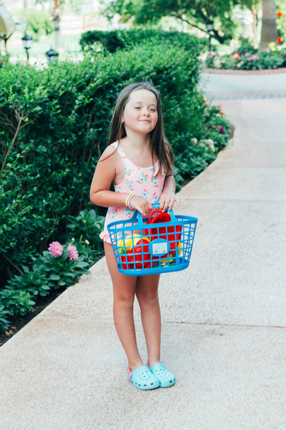 Linda chica caucásica bebé bronceado feliz con traje de baño con una cesta de juguetes de playa. Concepto vacaciones de verano
 - Foto, imagen