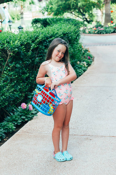 Mignon heureux bronzé bébé caucasien fille portant maillot de bain avec un panier de jouets de plage. Concept vacances d'été
 - Photo, image