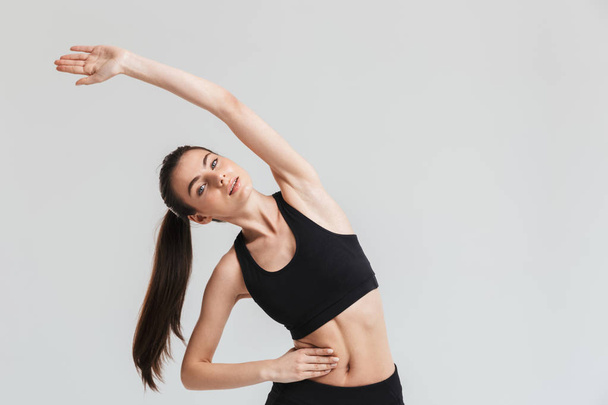 Beautiful young sport fitness woman make exercises isolated over grey wall background. - Foto, afbeelding