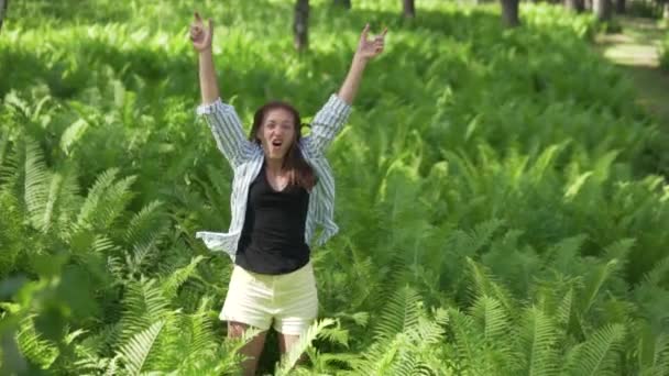 幸せな女性がジャンプし、シダの茂みの中で手を上げます. - 映像、動画