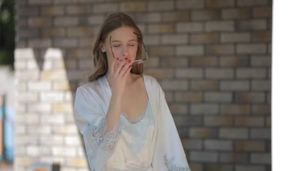 Beautiful model in peignoir wearing eyewear walking along luxury home yard - Кадры, видео