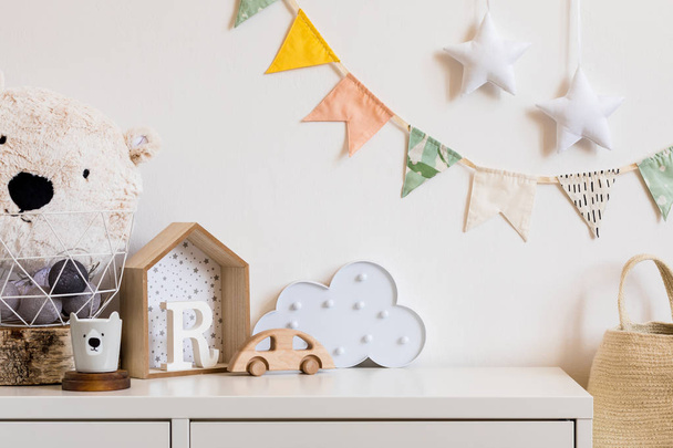Stylish scandinavian nursery interior with white teddy bear, wooden toys and star. Hanging cotton flags and natural basket on the white background wall. Cozy and sunny childroom. - Foto, afbeelding