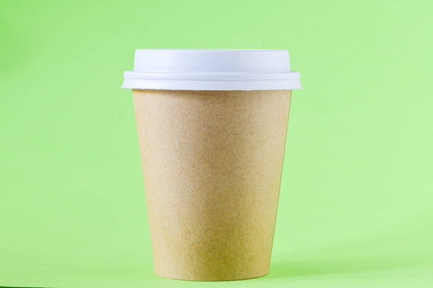 Close-up weergave van bruine papieren beker met koffie om op groene achtergrond te gaan - Foto, afbeelding