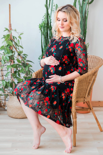 pregnant woman in a black dress sitting in a wicker chair - Фото, изображение