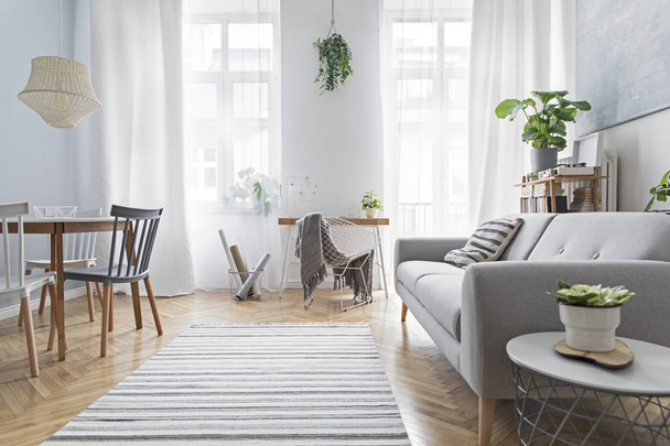 Moderna sala de estar escandinava con muebles de diseño, mesa familiar, plantas, librería de bambú y escritorio de madera. Parquet de madera marrón. Pintura abstracta en la pared blanca. Bonito apartamento
.  - Foto, imagen