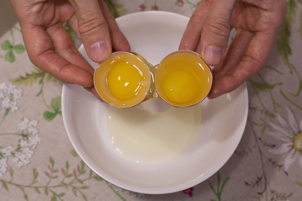 Dos yemas en un huevo. 2 en 1. Las manos de las mujeres abren un huevo único wi
 - Foto, imagen