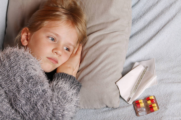 Больная девушка лежит в постели с термометром и лекарствами.
 - Фото, изображение