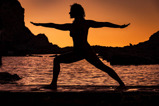 Jooga asema nuori tyttö rannalla auringonlaskun aikaan
 - Valokuva, kuva