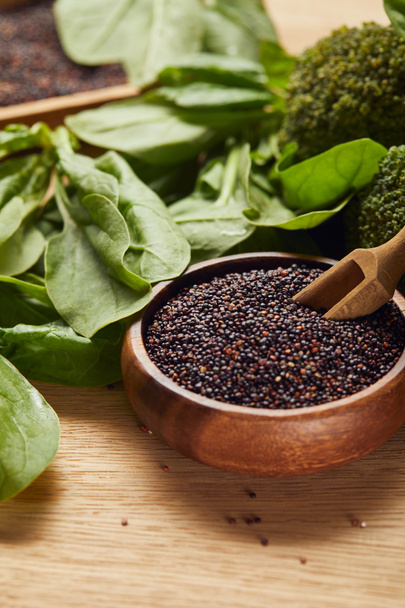 graines de quinoa noir dans un bol en bois avec spatule près des feuilles d'épinards verts
 - Photo, image