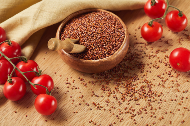 red quinoa in wooden bowl with spatula near beige napkin and tomatoes - Photo, Image