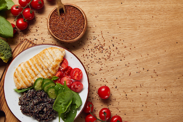 felülnézet főtt quinoa grillezett csirkemell és zöldség fehér lemez közelében nyers piros quinoa magok fa tál - Fotó, kép