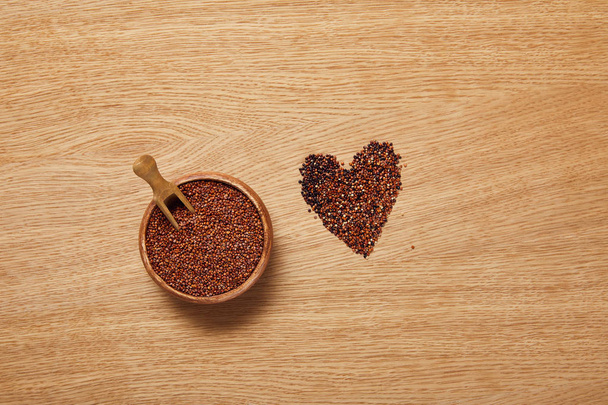 top view of red quinoa seeds in wooden bowl with spatula near heart sign - Фото, изображение