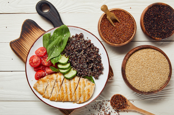 kaselerde çiğ kuru tohumlar ile beyaz ahşap masa üzerinde ızgara tavuk göğsü ve sebze ile pişmiş Quinoa üst görünümü - Fotoğraf, Görsel