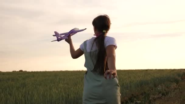 Gelukkig meisje loopt met een speelgoed vliegtuig op een tarwe veld. kinderen spelen speelgoed vliegtuig. tiener droomt ervan om te vliegen en piloot te worden. het meisje wil piloot en astronaut worden. - Video