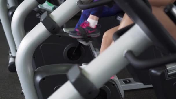 Two fitness females legs doing cardio workout on stationary cycle at gym. - Footage, Video