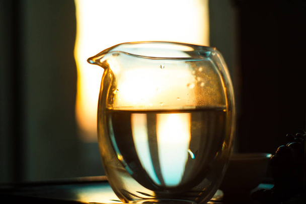 jarro de vidro de chá quente na mesa de madeira no fundo do belo pôr do sol com raios de sol
. - Foto, Imagem