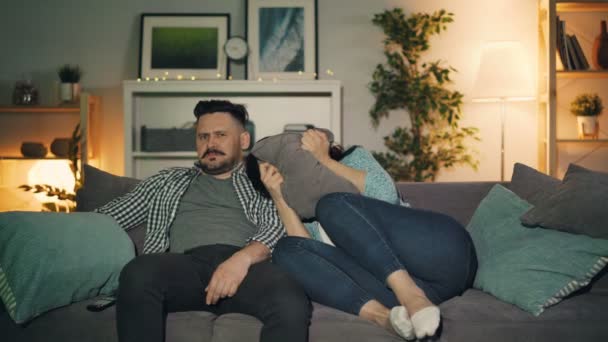 Man and woman watching shocking news on TV at home, guy comforting scared girl - Metraje, vídeo