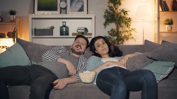 眠い女の子と男はテレビを見て、アパートで夜にポップコーンを食べて - 映像、動画