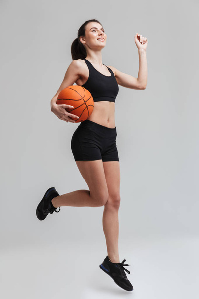 Young sport fitness woman player make exercises play basketball isolated over grey wall background. - Valokuva, kuva