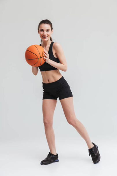 Young sport fitness woman player make exercises play basketball isolated over grey wall background. - Foto, Imagen