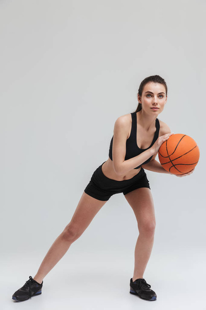 Young sport fitness woman player make exercises play basketball isolated over grey wall background. - Φωτογραφία, εικόνα
