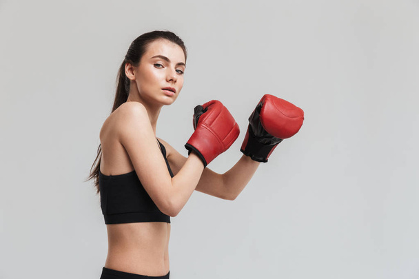 Young sport fitness woman boxer isolated over grey wall background make exercises in gloves. - Foto, afbeelding