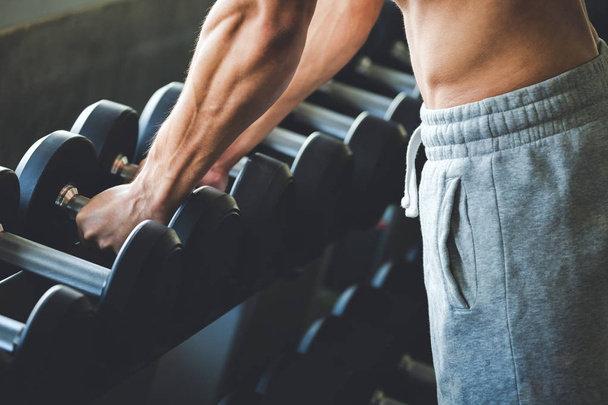 vista recortada del hombre de fitness haciendo ejercicios y levantamiento de pesas de mancuerna en el gimnasio deportivo
 - Foto, Imagen