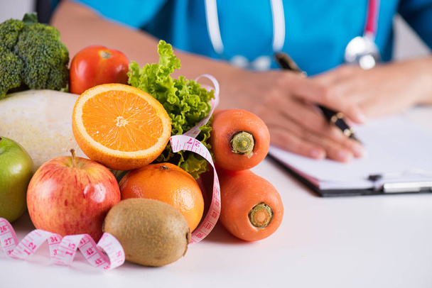 Estilo de vida saludable, comida y concepto nutricional. Primer plano de verduras y frutas frescas con estetoscopio acostado en el escritorio del médico
. - Foto, Imagen
