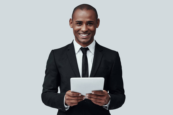 Business is his life. Charming young African man in formalwear working using digital tablet while standing against grey background - Photo, Image