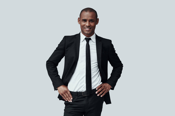 Her yönden mükemmel. Yakışıklı genç Afrikalı adam formalwear kamera bakıyor ve gri arka plan karşı dururken gülümsüyor - Fotoğraf, Görsel