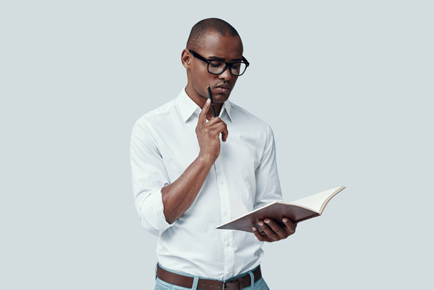 Student. Handsome young African man reading something while standing against grey background - Photo, Image