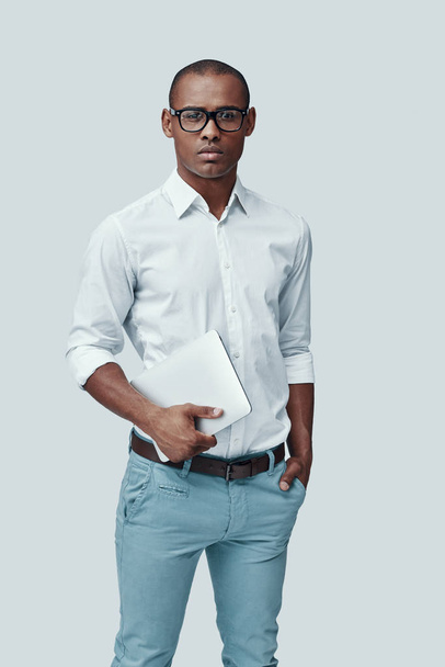 Довіри. Красивий молодий Африканський людина з використанням цифрової планшета і дивлячись на камеру, стоячи проти сірого фону - Фото, зображення