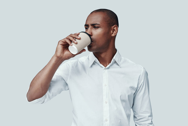 Poranna kawa. Przystojny młody afrykański mężczyzna picie kawy stojąc na szarym tle - Zdjęcie, obraz