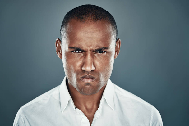 Feeling furious. Displeased young African man in shirt looking at camera and frowning while standing against grey background - Photo, Image