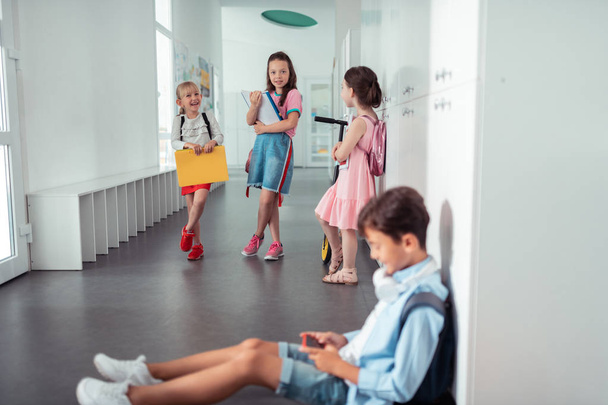 Girls standing and looking at boy sitting on the floor at school - Photo, Image
