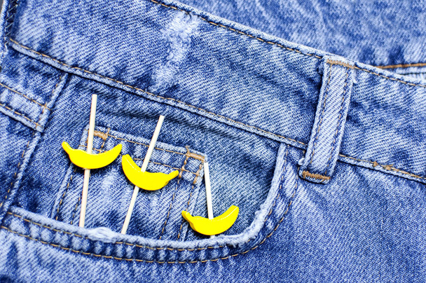 Niebieskie dżinsy i żółte drewniane banany z kieszeni na czarnym tle góry widok płaski lay. Szczegóły ładne niebieskie dżinsy. Dżinsy tekstury lub denim tle. Odzież trend. Moda, selektywna ostrość - Zdjęcie, obraz